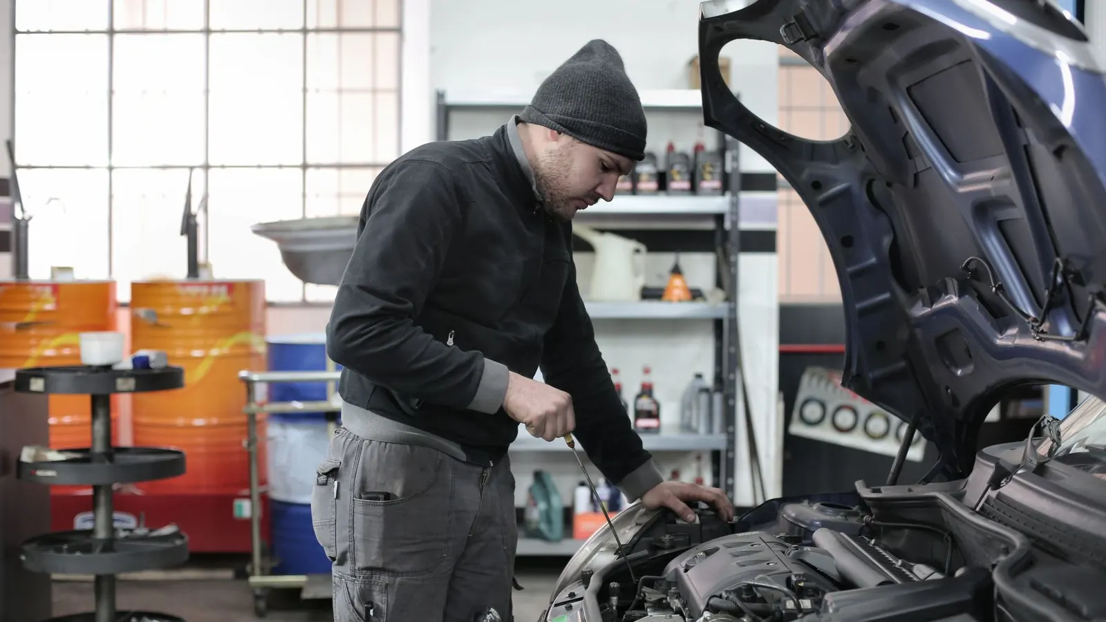 Automechanik pracuje pod otvorenou kapotou auta v dielni, web pre autoservis