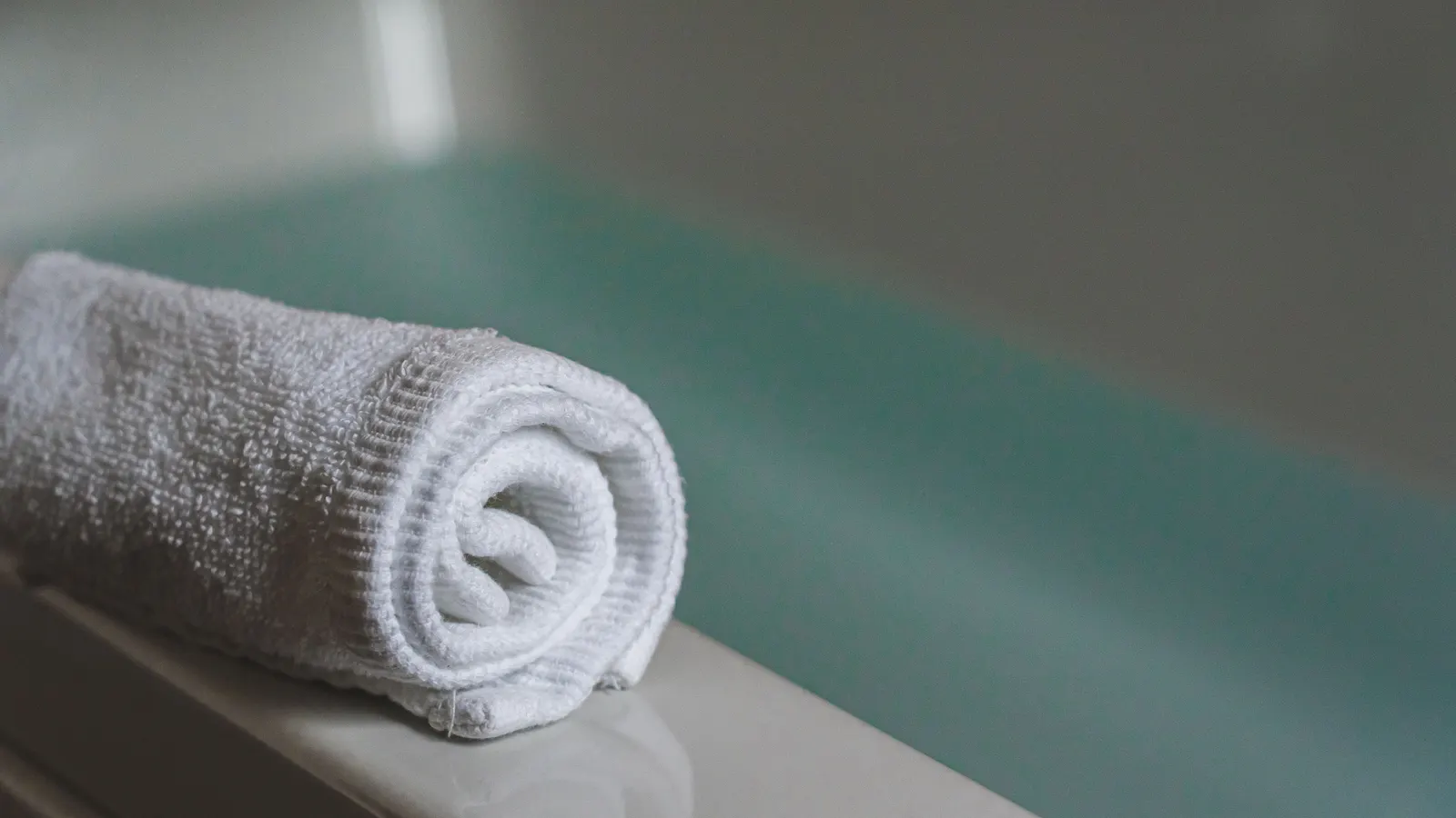 Zrolovaný biely uterák pri vani, wellness atmosféra salónu, web pre kaderníctvo